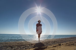 Woman stands ashore opposite sun