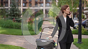 A woman stands with a baby stroller on the sidewalk and talks on a mobile phone.