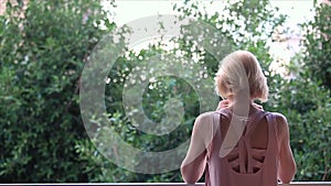 A woman stands on the balcony and enjoys the peace and the view of the lush greenery in the early summer morning