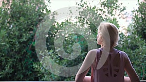 A woman stands on the balcony and enjoys the peace and the view of the lush greenery in the early summer morning