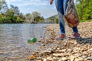 A woman stands on the Bank of the hand with a garbage bag, and a bottle lying in the water. The concept of the protection of the