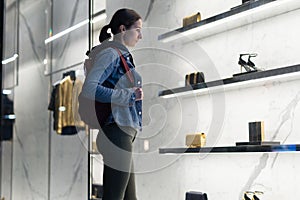 Woman stands at a boutique window and looks at shoes.