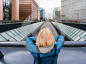 A woman stands on a bridge with her back to the camera against the background of a modern office quarter, Belgium