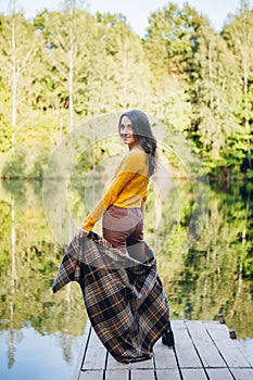 Woman stands on a bridge on a lake with an autumn landscape