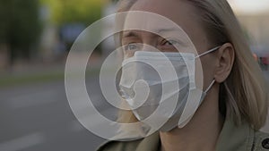 A woman stands at a bus stop in the city center, puts a medical mask on her face.