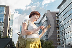 Woman stands in a business city district and looks at the screen of smartphone