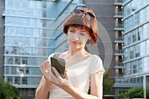 Woman stands in a business city district and looks at the screen of smartphone