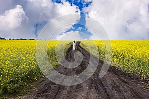 woman stands on a dirt road in a rapeseed field