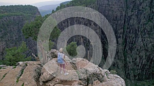 A woman stands on the edge of the cliff and admires the beautiful view of the mountain gorge.