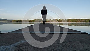 A woman stands at the end of a dock on a still morning at the lake