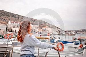 A woman stands in front of a row of boats, some of which have orange life preservers on them. The scene is peaceful and photo