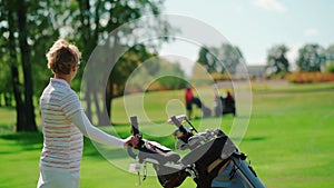 Woman stands on the golf course and holds a cart with golf equipment in her hand