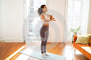 woman stands in her living room, hands clasped in meditation