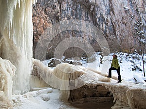 A woman stands on the ice near a waterfall