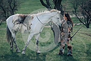 Woman stands in image of warrior amazon with bow in her hands near her horse