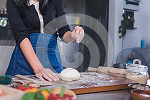 A woman stands in the kitchen and uses her hands to rub flour. which is the process of making pizza