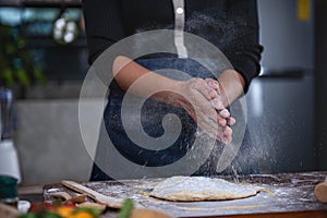 A woman stands in the kitchen and uses her hands to rub flour. which is the process of making pizza
