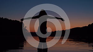 Woman Stands Knee-Deep In The Water Of The Lake At Sunset Raises Her Arms Up