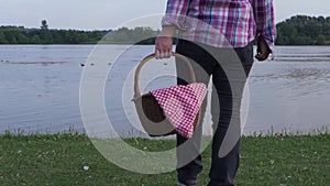 Woman stands by lake shore with vintage picnic basket