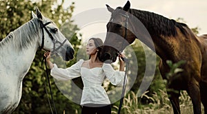 Woman stands near two horses and holds them by bridle