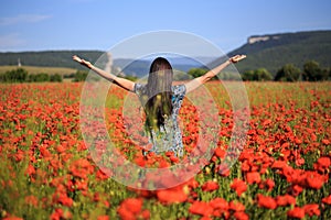 Woman stands with open arms on summer poppy field