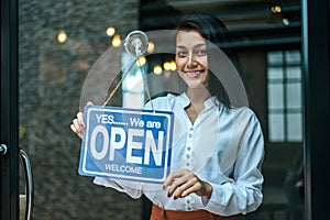 Woman  stands and opens a wide sign through the shop window and smile