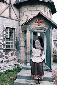 A woman stands praying at the door of an old catholic church