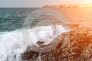 A woman stands on a rock in the sea during a storm. Dressed in a white long dress, the waves break on the rocks and