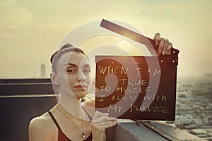 Woman stands on the roof with a poster `When I am true to myself, I align with my purpose` International Womens Day  concept.