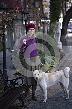 A woman stands in the street with a stray dog.