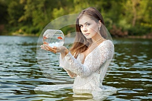 Woman stands in water, in her hands a goldfish.