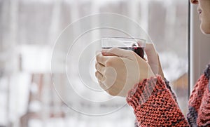 A woman stands at the window with a cup of mulled wine in his hand
