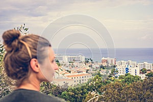 A woman stares into the distance to the sea horizon and the city in front of him