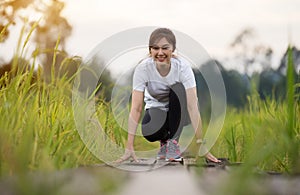 Woman in starting position ready for running on wooden path in field