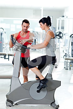 Woman on stationary bicycle with personal trainer