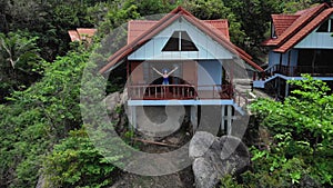Woman stays at bungalow balcony and looking to the sea. Aerial shot. Quadcopter is flying to young girl which is looking
