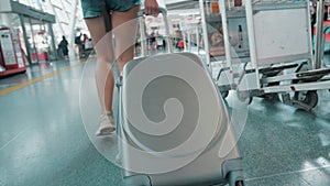 Woman stepping and roll suitcase on wheels. Woman walking with her suitcase along airport. Travel concept. Slow motion