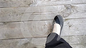 A woman steps cautiously on an old wooden bridge. Legs top view