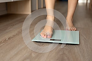 A woman steps on the scales to measure her weight at home, leg close-up.