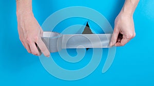 Woman sticking silver tape on a hole on a blue background.