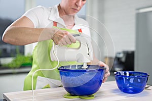 Woman is stirring dough in a blueish bowl in her modern kitchen