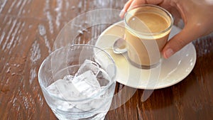 Woman stirring an espresso with a drop of milk and pouring it into a glass with ice