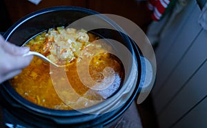 Woman stirring with a plastic scoop the soup with meatballs cooked in a slow cooker
