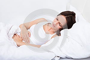 Woman with stomach ache lying on bed photo
