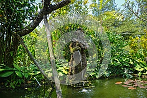 A woman stone statue on the garden park bali pouring water on the lake with green tree and grass on background - photo