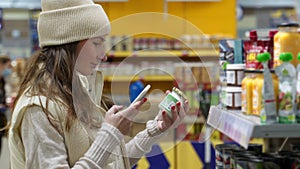 Woman in a store checks the nutrients of canned food on a smartphone by scanning a barcode