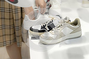 A woman in the store looks White sneakers before buying a new shoe. Gray sneakers in the foreground