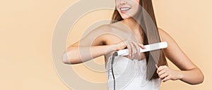 Woman straightening hair with straightener. Portrait of young beautiful girl using styler on her shining hair. Hairstyle