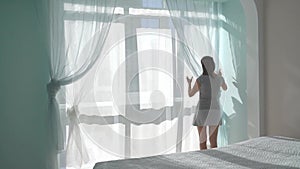 Woman straightens tulle on beautiful panoramic window, home cleaning, cozy house, step 1