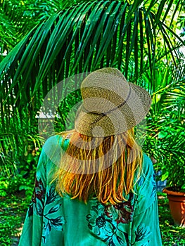 A woman with straw hat on backside with palms